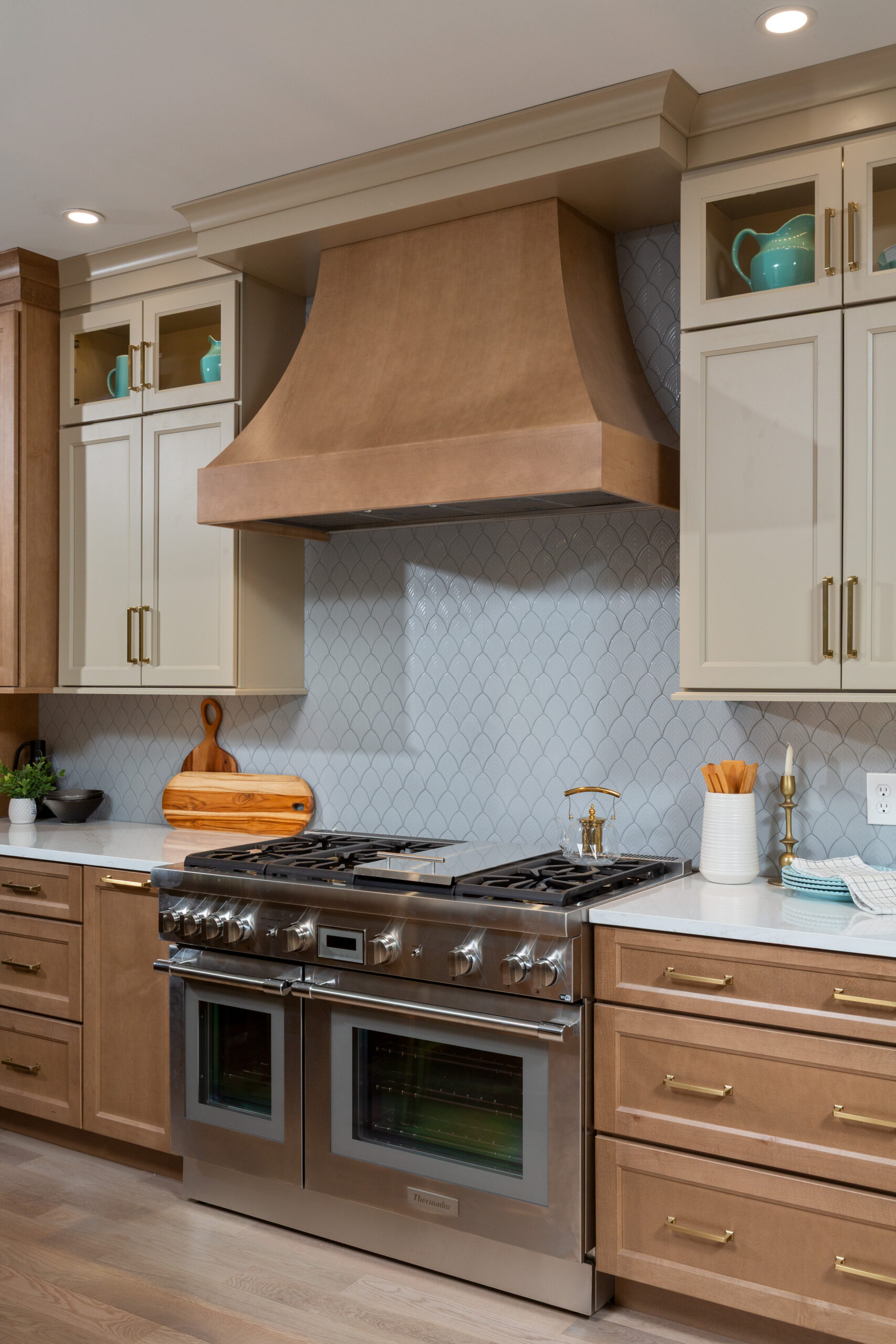 Custom wood range hood over stainless steel gas range with patterned tile backsplash.